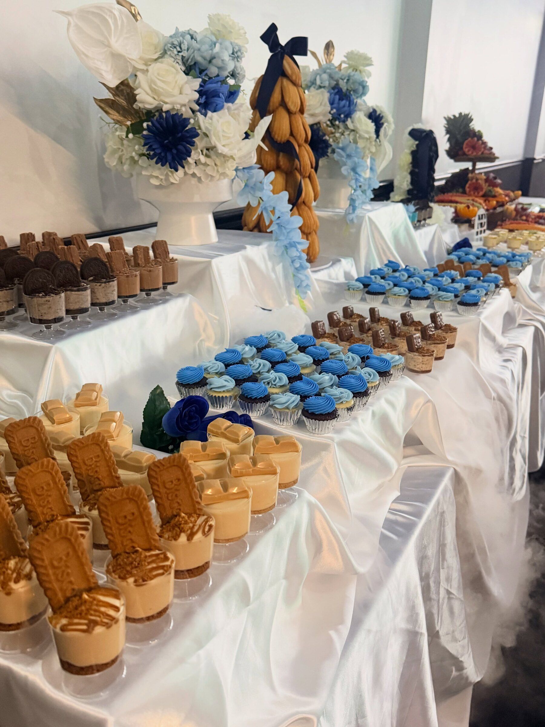 A blue-themed dessert table with satin draping, cupcakes and dessert cups